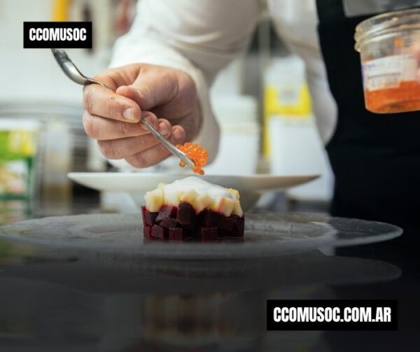 Un chef emplata un bocado con huevas naranjas sobre un plato negro