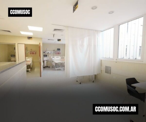 Sala de hospital con varias camas y equipos médicos, separadas por cortinas blancas