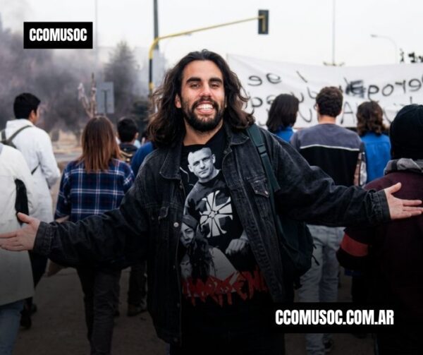 Darío Santillán sonriente con los brazos abiertos en una protesta callejera, con gente y pancarta al fondo