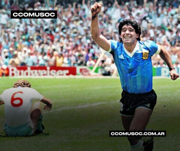 Futbolista argentino celebrando un gol con el puño en alto, mientras un rival está sentado en el césped