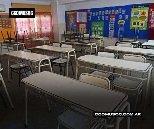 Aula vacía con pupitres y sillas apiladas sobre las mesas, con carteles educativos en la pared